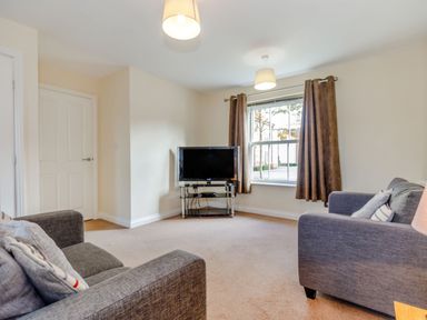 A living room with two sofas a television on a stand and a window with curtains at Perriwinkle The Bay near Filey