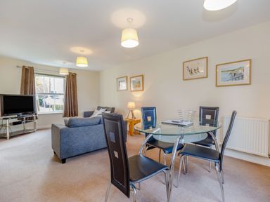 An open living and dining area with a glass dining table and four chairs two sofas a television on a stand and framed pictures on the wall at Perriwinkle The Bay near Filey