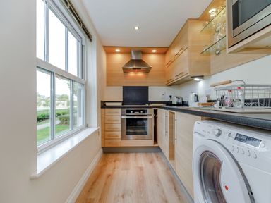 A kitchen with wooden cabinets a washing machine an oven and a large window at Perriwinkle The Bay near Filey
