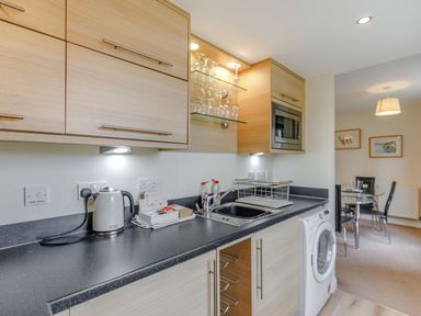 A kitchen counter with a kettle sink washing machine and glass shelves at Perriwinkle The Bay near Filey