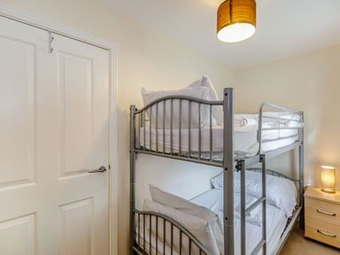 A bedroom with metal bunk beds a wooden nightstand with a lamp and a closed white door at Perriwinkle The Bay near Filey