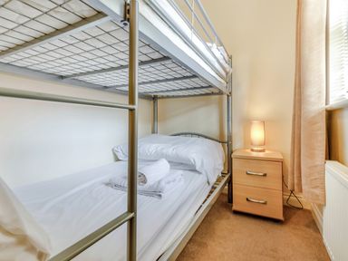 A bedroom with a metal bunk bed and a wooden nightstand with a lamp at Perriwinkle The Bay near Filey