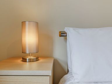 A bedside table with a turned on lamp next to a bed with a white pillow at Perriwinkle The Bay near Filey