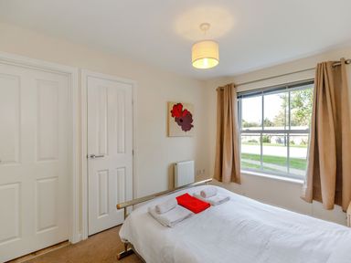 A bedroom with a bed with white bedding and towels ceramic curtain by window and two closed white doors at Perriwinkle The Bay near Filey