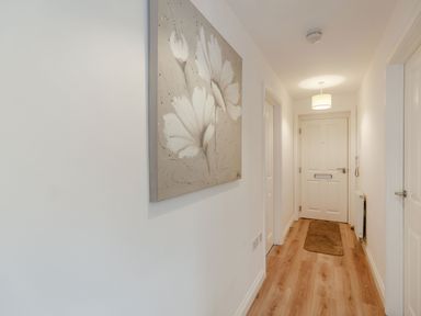 A hallway with wooden floor a front door a brown rug a wall painting of white flowers and ceiling light at Perriwinkle The Bay near Filey