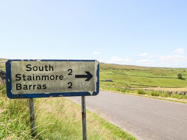 A road sign showing directions to South Stainmore and Barras on a rural road surrounded by grassy fields at The Cow Byre in Barras near Kirkby Stephen