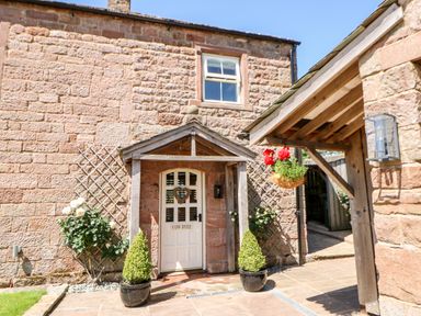 The stone exterior of a building with a white door and two potted plants on either side at The Cow Byre in Barras near Kirkby Stephen