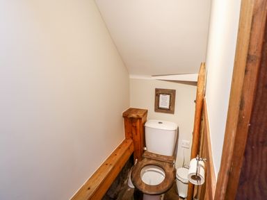 A small bathroom with a wooden toilet seat and a toilet paper holder on the wall at The Cow Byre Barras near Kirkby Stephen