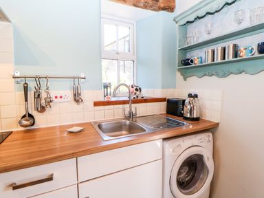 A kitchen sink washing machine and teal shelf with cups and glasses at The Cow Byre in Barras near Kirkby Stephen