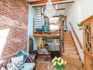 A living area with exposed brick wall wooden stairs chandelier and kitchen at The Cow Byre Barras near Kirkby Stephen