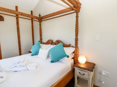 A bedroom with a wooden four-poster bed blue and white pillows white towels on bed and a bedside table with a lamp at The Cow Byre in Barras near Kirkby Stephen