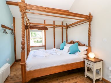 A bedroom with a four-poster wooden bed blue pillows and a side table with a lamp at The Cow Byre Barras near Kirkby Stephen