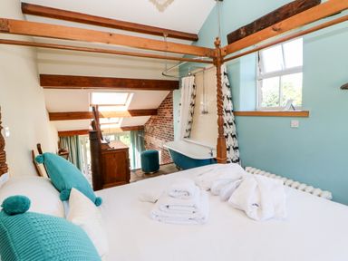 A bedroom with a four-poster bed towels and bathrobes a bathtub with a shower curtain and wooden beams at The Cow Byre in Barras near Kirkby Stephen