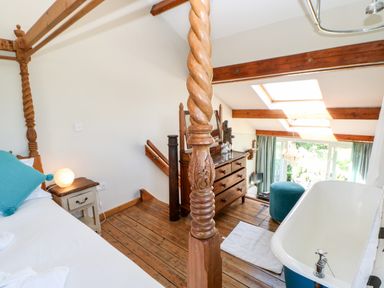 A bedroom with a four-poster bed a bathtub wooden dresser and skylights at The Cow Byre in Barras near Kirkby Stephen
