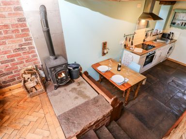 A kitchen with a wood stove and a small dining table set for two at The Cow Byre Barras near Kirkby Stephen