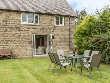 A garden with a glass table and six chairs next to a stone house with open doors at Stephen's Cottage in Alnmouth