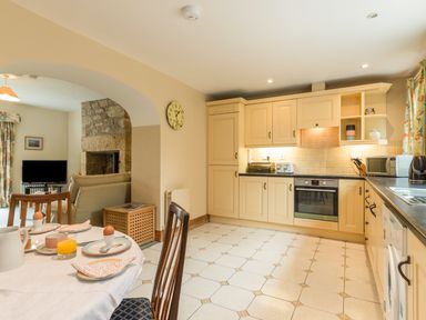 A kitchen with cream cabinets a dining table set with breakfast and an archway leading to a living room at Stephens Cottage in Alnmouth