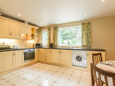 A kitchen with beige cabinets a washing machine a microwave and a dining table at Stephens Cottage in Alnmouth