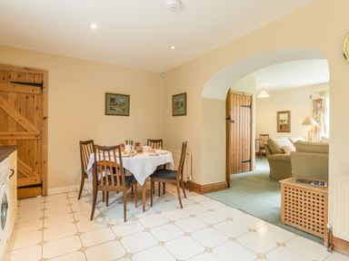 A dining area with a wooden table and chairs and an adjoining living room with sofas at Stephens Cottage in Alnmouth
