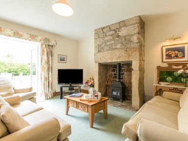 A living room with beige sofas a wooden coffee table a stone fireplace and a television at Stephens Cottage in Alnmouth