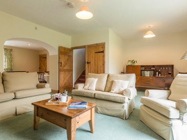 A living room with beige sofas a wooden coffee table and a wooden cabinet at Stephens Cottage in Alnmouth