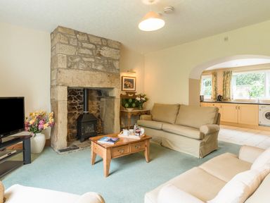 A living room with sofas a stone fireplace a wooden coffee table and a television next to an open kitchen at Stephens Cottage in Alnmouth