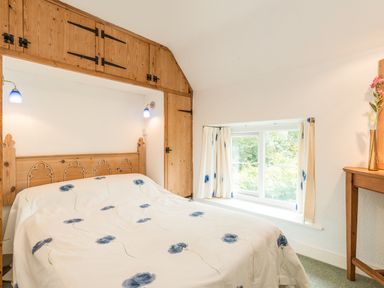 A bedroom with a bed covered in floral bedding wooden built-in cupboards and a window with curtains at Stephens Cottage in Alnmouth