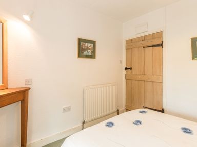 A bedroom corner with a wooden door a radiator a wooden table with a mirror and a bed with a floral duvet at Stephens Cottage in Alnmouth
