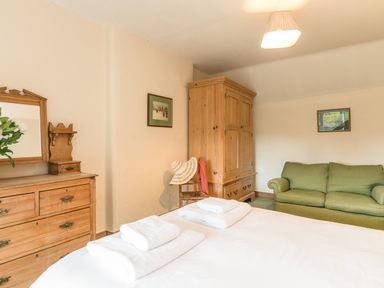 A bedroom with a wooden dresser and mirror a wooden wardrobe a green sofa and a bed with folded towels at Stephens Cottage in Alnmouth