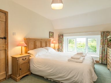 A bedroom with a wooden bed and bedside tables with lamps and a window with curtains at Stephen's Cottage in Alnmouth