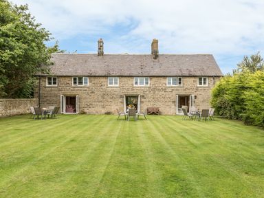 A stone house with open doors and garden chairs and tables on a lawn at Stephens Cottage in Alnmouth