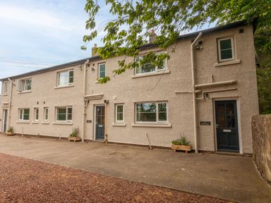The exterior of a beige two story building with multiple windows and two blue doors with flower boxes at Stephen's Cottage in Alnmouth