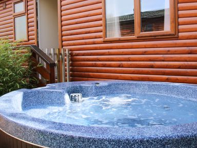 An outdoor hot tub with bubbling water beside a wooden cabin with windows and a small fence