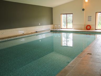 An indoor swimming pool with tiled walls and floor and windows showing outdoor trees at Oak Lodge in Beaconsfield Holiday Park