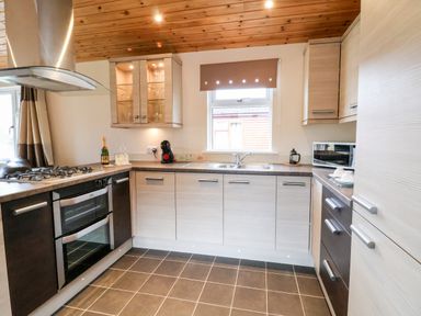 A kitchen with a stove, oven, sink, countertop appliances, cabinets, and tiled floor at Oak Lodge in Beaconsfield Holiday Park