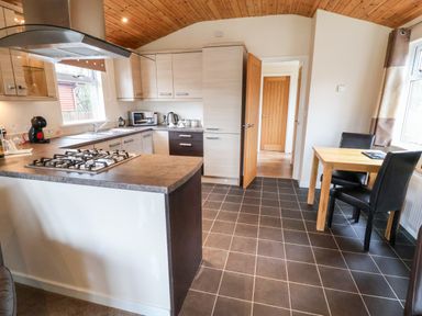 A kitchen with a gas stove island wooden ceiling dining table and black chairs at Oak Lodge Beaconsfield Holiday Park
