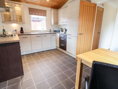 A kitchen with counters cabinets a stove a microwave a sink a wooden table and a chair at Oak Lodge Beaconsfield Holiday Park