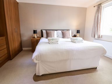 A bedroom with a double bed bedside tables with lamps and folded towels on the bed at Oak Lodge Beaconsfield Holiday Park