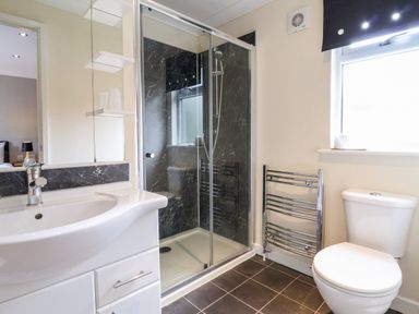 A bathroom with a sink and cabinet a glass shower enclosure a toilet and a towel radiator at Oak Lodge in Beaconsfield Holiday Park