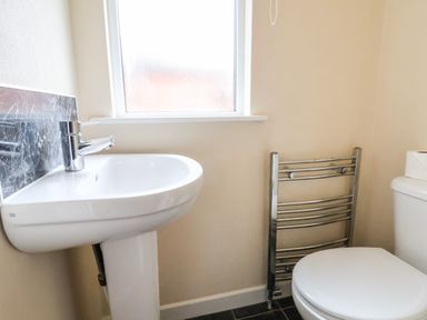A bathroom with a white pedestal sink a toilet a metal towel rail and a frosted window at Oak Lodge in Beaconsfield Holiday Park