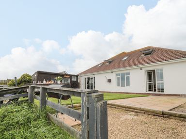 A backyard with a patio table set with glasses and food a charcoal grill and a white house with an open door at On The Watersedge in Beadnell