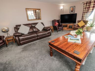 A living room with brown leather sofa armchairs wooden coffee table and a television at On The Watersedge in Beadnell