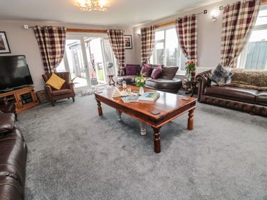 A living room with leather sofas a wooden coffee table a television and checkered curtains at On The Watersedge in Beadnell