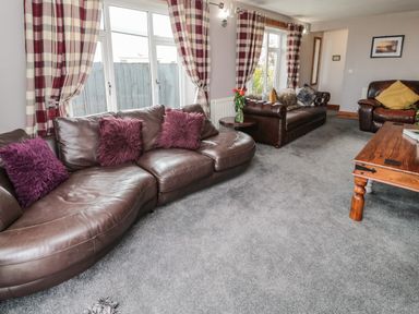 A living room with leather sofas purple cushions checked curtains and a wooden coffee table at On The Watersedge in Beadnell