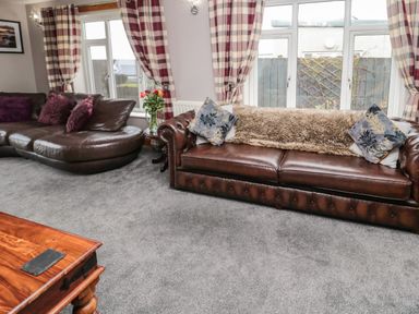A living room with two brown leather sofas, a wooden coffee table, plaid curtains, and windows at On The Watersedge in Beadnell