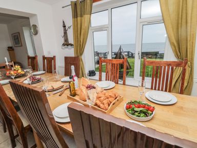 A dining room with a wooden table set with plates glasses and food in front of windows with yellow curtains at On The Watersedge in Beadnell