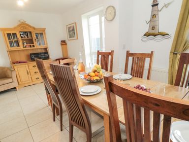 A dining room with a wooden table and chairs fruit bowl wall clock and wooden cabinet at On The Watersedge in Beadnell