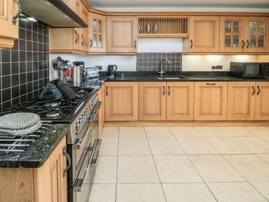 A kitchen with wooden cabinets a black countertop a stove a sink and various appliances at On The Watersedge Beadnell