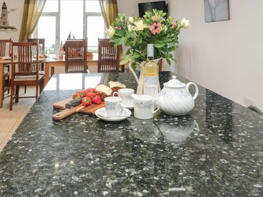 A kitchen island with flowers tea set cake and strawberries and a dining table with chairs in the background at On The Watersedge in Beadnell