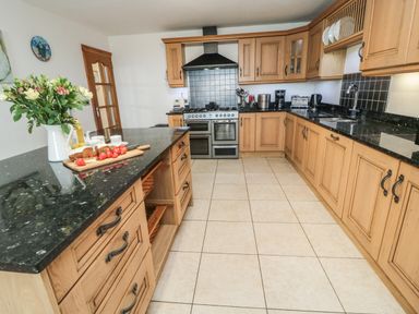 A kitchen with wooden cabinets a black countertop a stove and a vase with flowers on the island at On The Watersedge in Beadnell